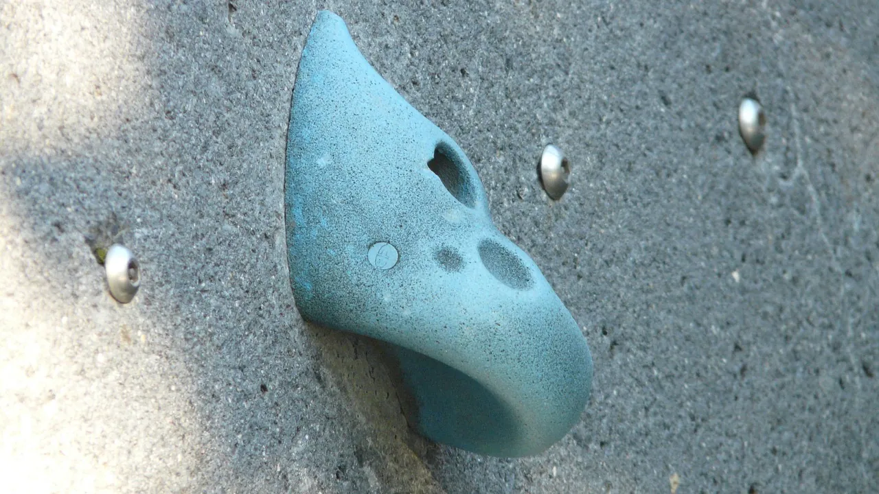 Une prise d'escalade bleue en lumière rasante, sur un mur d'entraînement